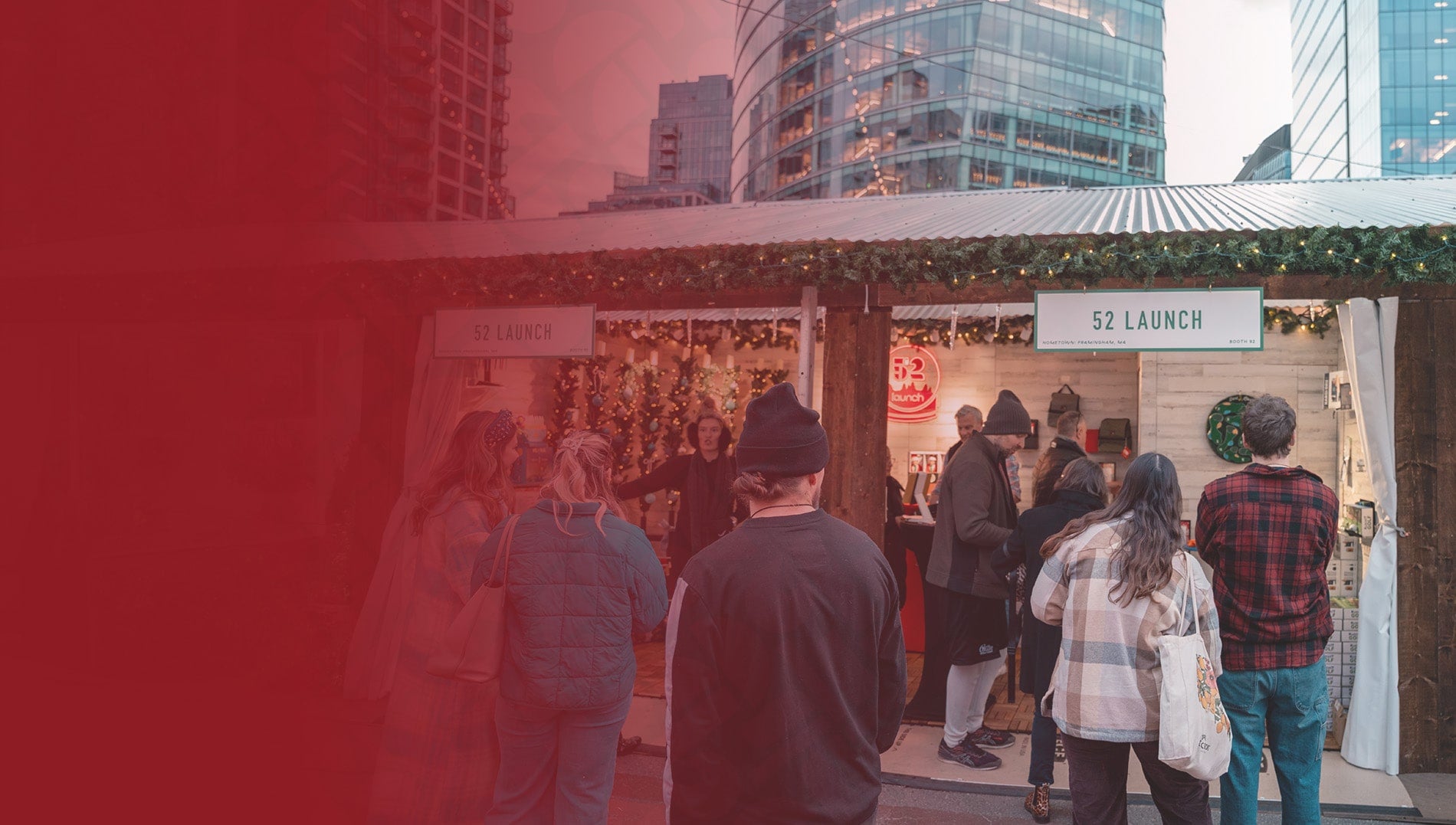 People gathered around a festive outdoor market stall with a city skyline in the background.